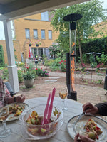 Selskab spiser under en veranda, mens en udendørs pilleovn brænder i haven