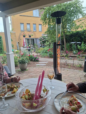 Selskab spiser under en veranda, mens en udendørs pilleovn brænder i haven